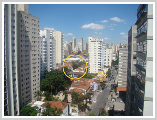 Paisagem urbana ensolarada, altos edifícios, círculo amarelo destaca área de casas ao centro