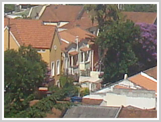 Fachada de uma casa e dois sobrados germinados com varanda, meio a árvores