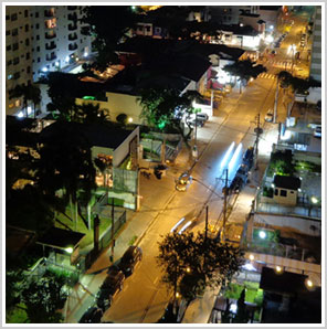 Foto noturna de rua: casas, árvores, rastros de carros em movimento