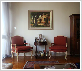 Duas poltronas avermelhadas, quadro, mesinha com vaso e porta-retratos, cores reais